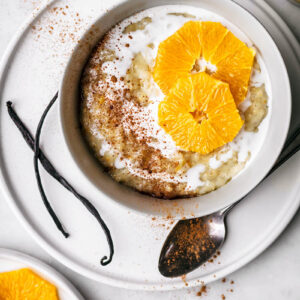 Top down view of a bowl of rice pudding topped with milk and orange slices.