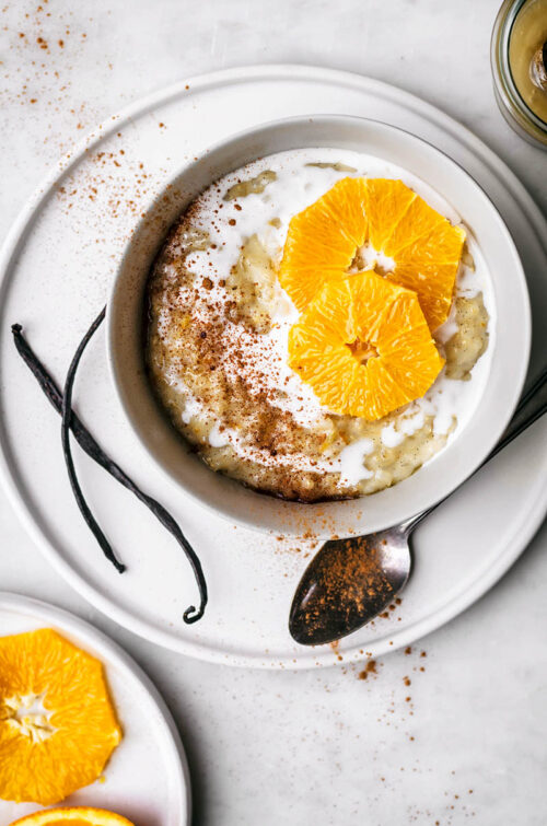 Top down view of a bowl of rice pudding topped with milk and orange slices.