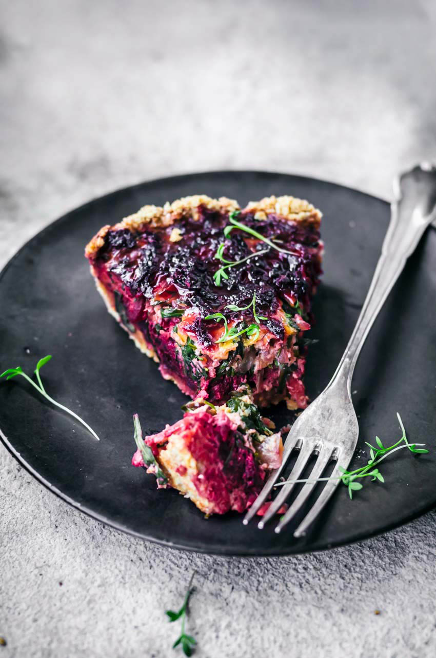 Beet tart slice on black plate, with fork and one bite cut.