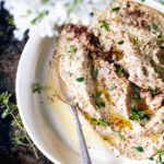 Top-down view of a pale spread or dip in a shallow bowl with sumac and thyme.