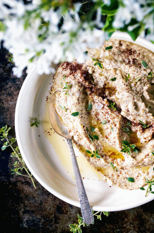 Top-down view of a pale spread or dip in a shallow bowl with sumac and thyme.