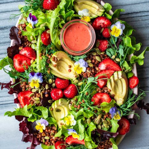 Strawberry salad with edible flowers, avocado, and lentils on a large platter.