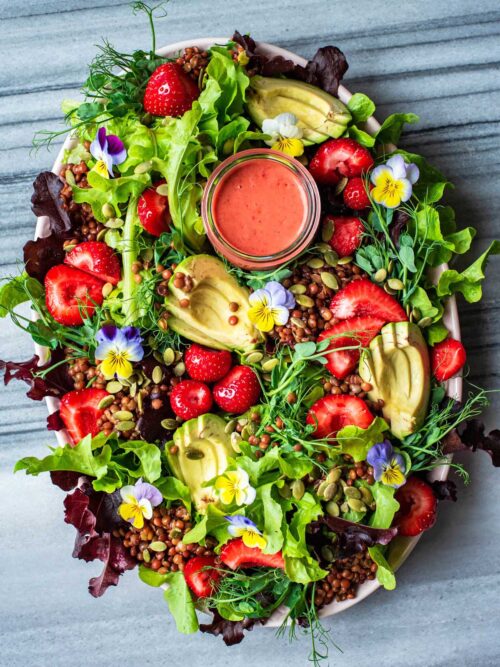 Strawberry salad with edible flowers, avocado, and lentils on a large platter.