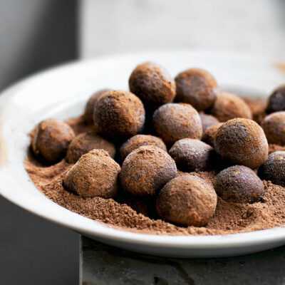 A plate full of date balls with cocoa powder.