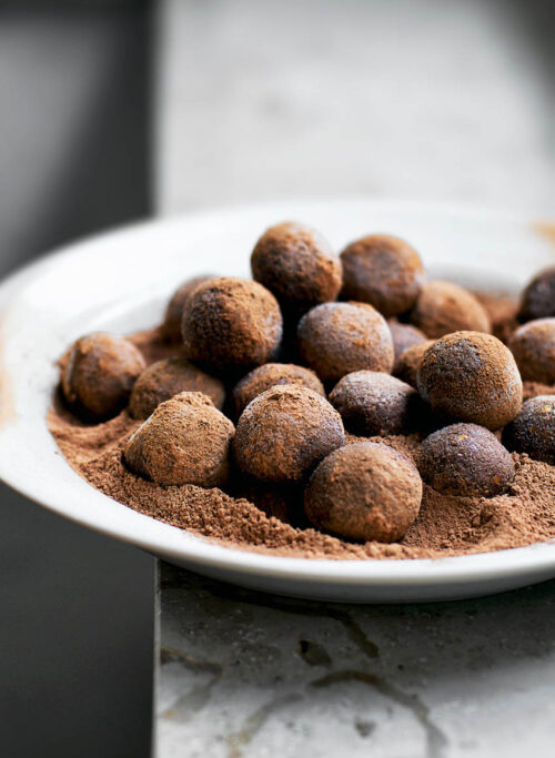 A plate full of date balls with cocoa powder.