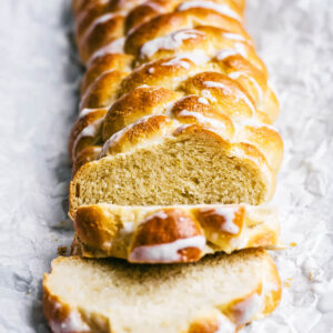 A six-strand bread, with three slices cut at the front, topped with a white glaze.