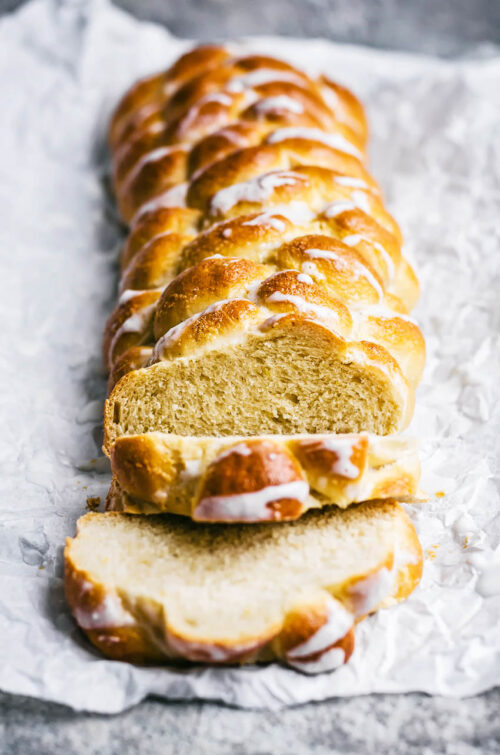 A six-strand bread, with three slices cut at the front, topped with a white glaze.