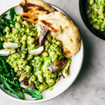 White bean salad with green sauce in a bowl with greens, naan, and cooked shallots.