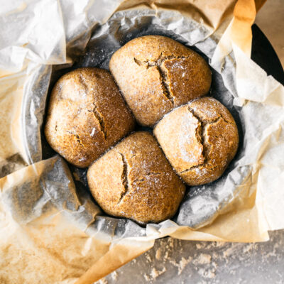 Four crusty buns with cracked tops in parchment lined cast iron pan, on marble surface