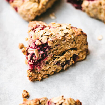 Close up of oatmeal raspberry scones on white paper, topped with extra oats.