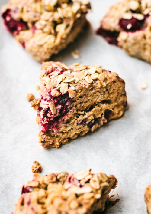 Close up of oatmeal raspberry scones on white paper, topped with extra oats.