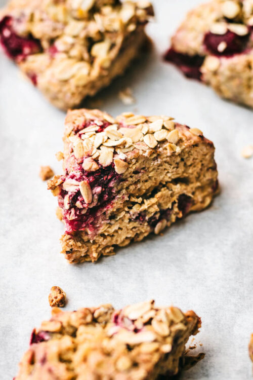 Close up of oatmeal raspberry scones on white paper, topped with extra oats.