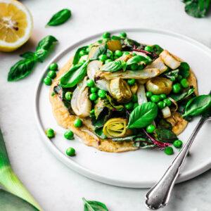 A chickpea flour pancake topped with a pile of spring vegetables.