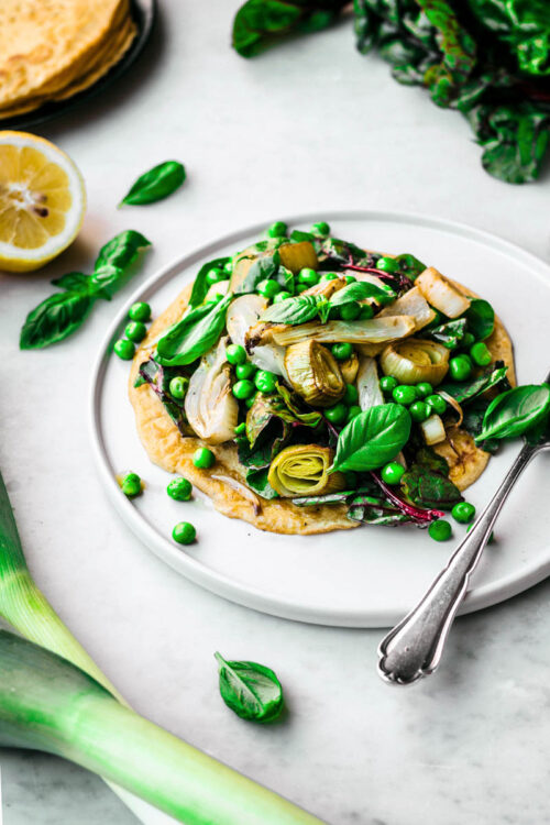 A chickpea flour pancake topped with a pile of spring vegetables.