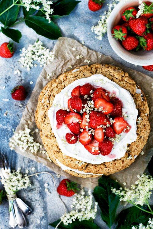 A large scone cake topped with whipped cream, strawberries, and elderflower blossoms.