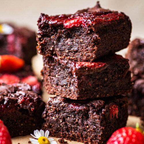 A stack of three brownies with strawberries around.