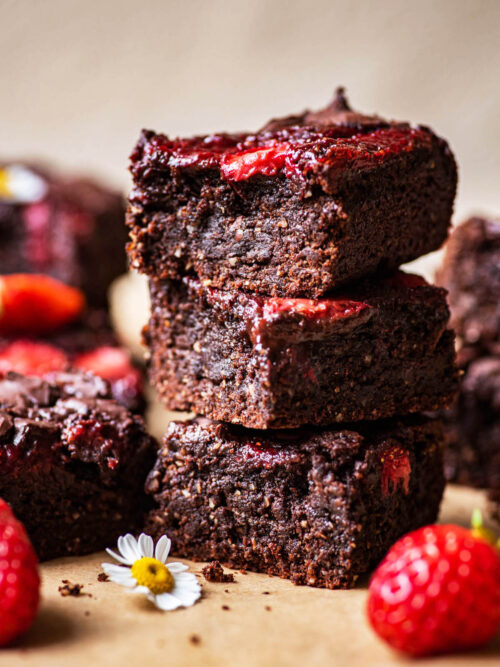 A stack of three brownies with strawberries around.