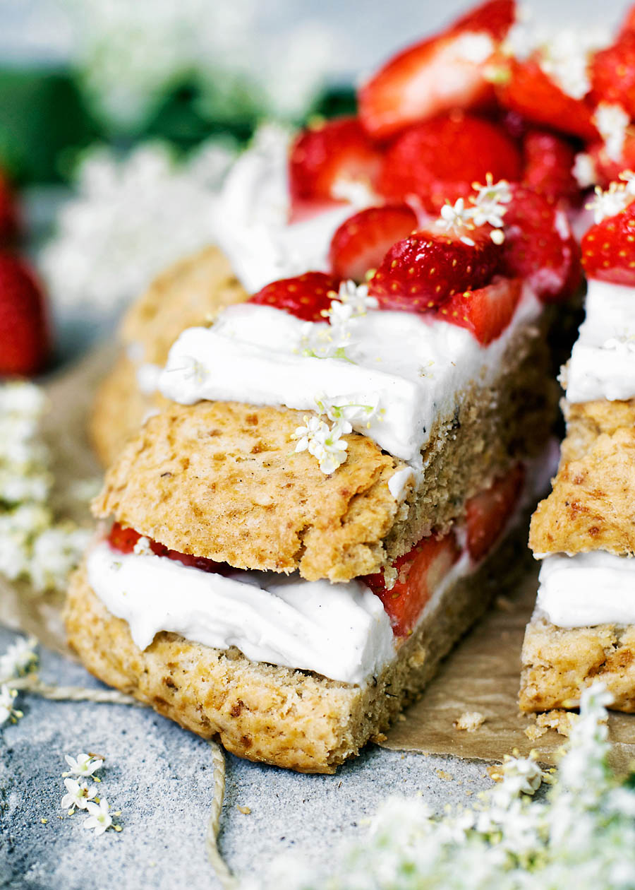 A slice of a large strawberry shortcake with cream and elderflower blossoms.
