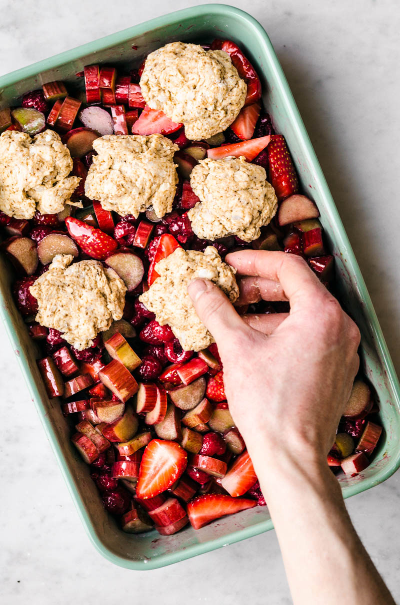 Woman's hand placing a biscuit onto a baking dish filled with fruit.