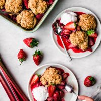 Strawberry rhubarb cobbler on two plates with spoon and scoop of ice cream.