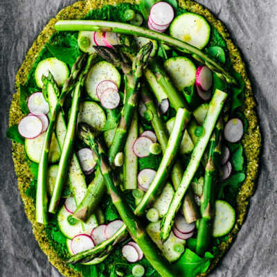 Broccoli flatbread topped with asparagus, radishes, zucchini, greens, spring onion, and pesto.