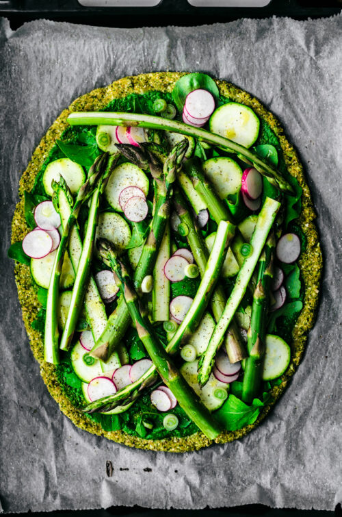 Broccoli flatbread topped with asparagus, radishes, zucchini, greens, spring onion, and pesto.