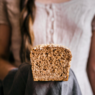 Woman holding loaf of bread, sliced side forward.