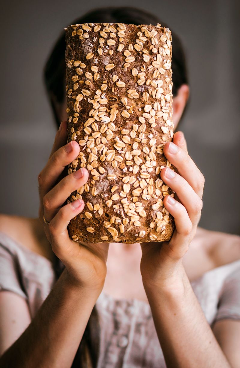 Woman holding honey oat bread in front of her face, top out.