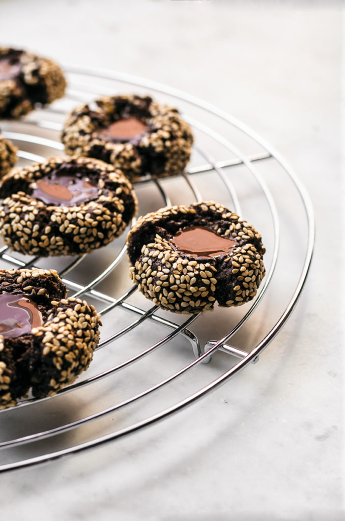 Chocolate thumbprint cookies with sesame seeds and melted chocolate centre on rack.