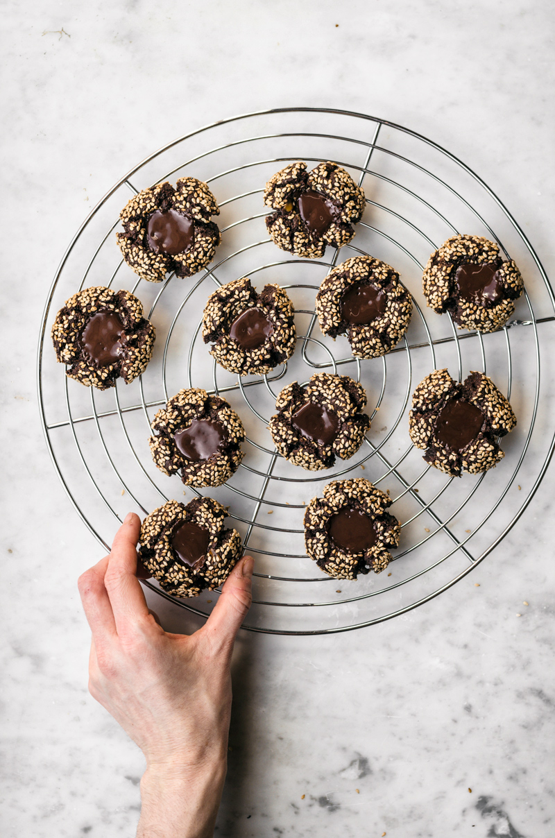 Chocolate thumbprint cookies with sesame seeds and melted chocolate centre on rack.