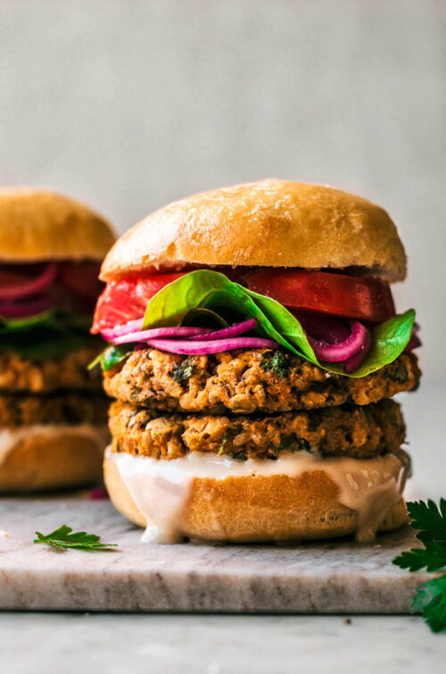 Close up of a veggie burger with double stacked patties and vegetable toppings.