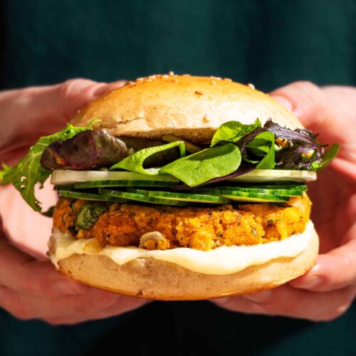 Woman's hands holding a veggie burger with green vegetable toppings.