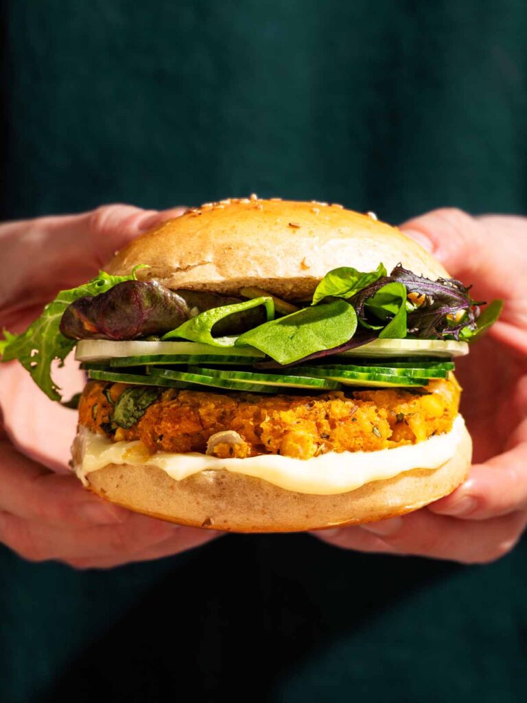 Woman's hands holding a veggie burger with green vegetable toppings.