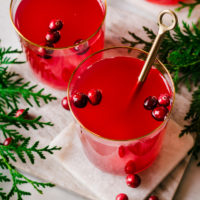 Glasses of cranberry tea, with berries floating in the glasses, and spoon in one cup.