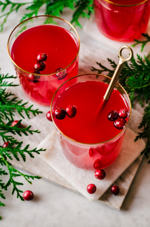 Glasses of cranberry tea, with berries floating in the glasses, and spoon in one cup.