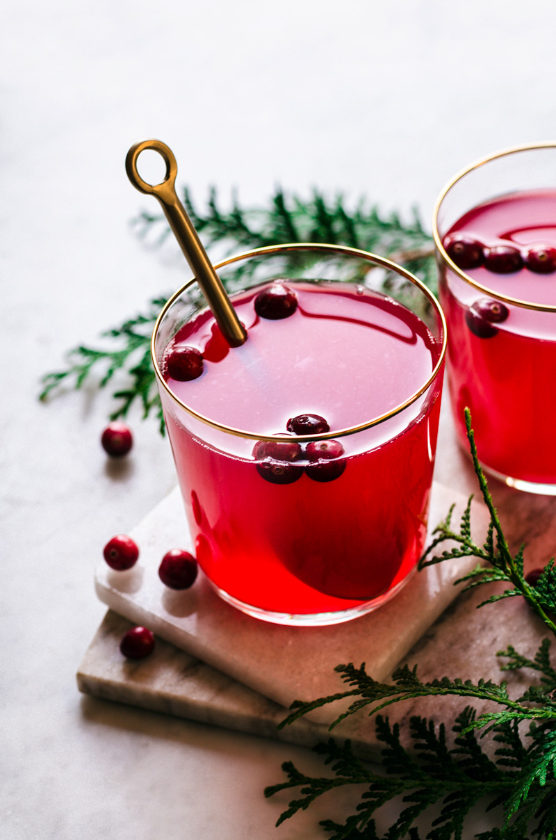 Glasses of cranberry tea, with berries floating in the glasses, and spoon in one cup.