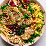 Roasted cauliflower steaks in a large bowl with preserved lemon, pomegranate, saffron rice, and black lentils.