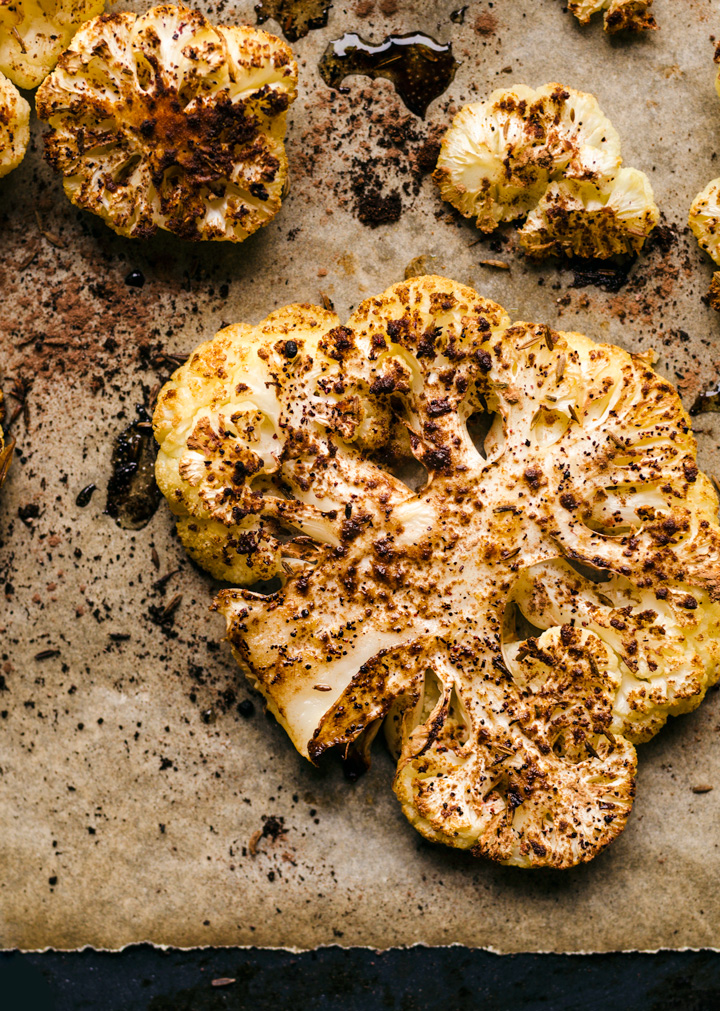 Roasted cauliflower steaks on a baking sheet with spices.
