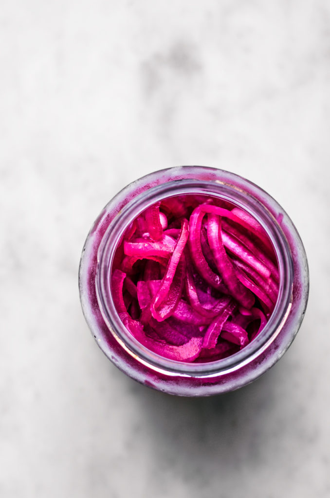 A jar of bright pink pickled red onions, top down view.