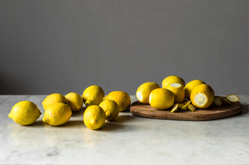 Several lemons on a marble board with a wooden cutting board.