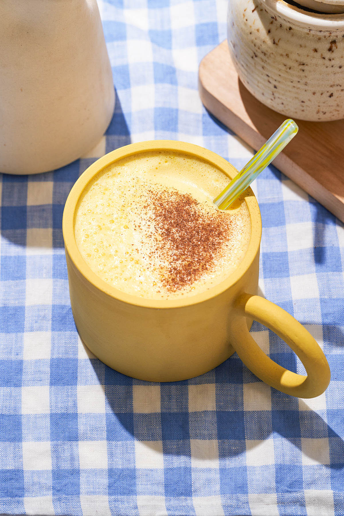 Yellow cup of a yellow drink on a blue gingham cloth.