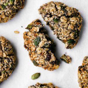Oatmeal cookie with seeds, broken in half, surrounded by other cookies.