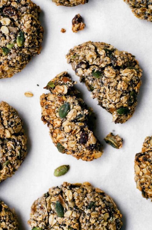 Oatmeal cookie with seeds, broken in half, surrounded by other cookies.