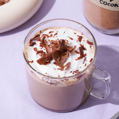 Hot chocolate in a glass mug with whipped cream and chocolate.