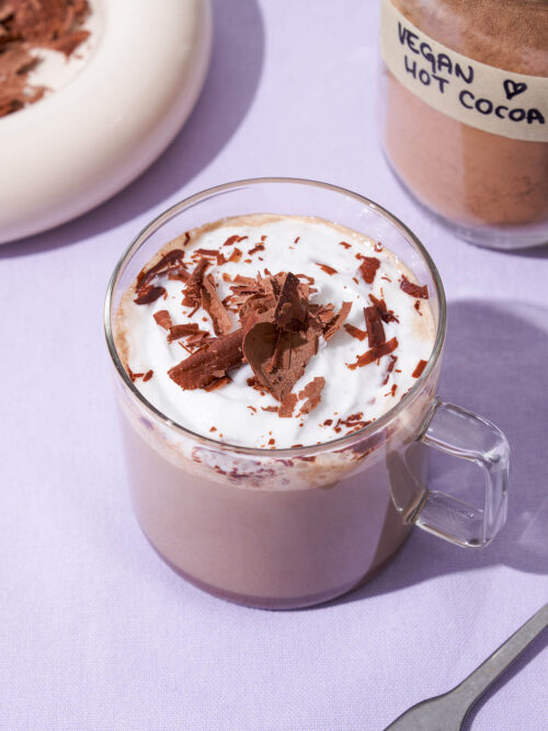 Hot chocolate in a glass mug with whipped cream and chocolate.