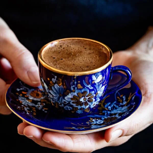 A small cup of coffee in a decorated blue cup with plate.