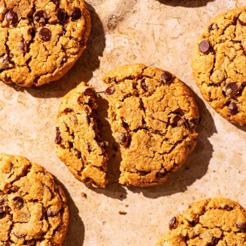 Several chocolate chip cookies on parchment paper, one broken in half.
