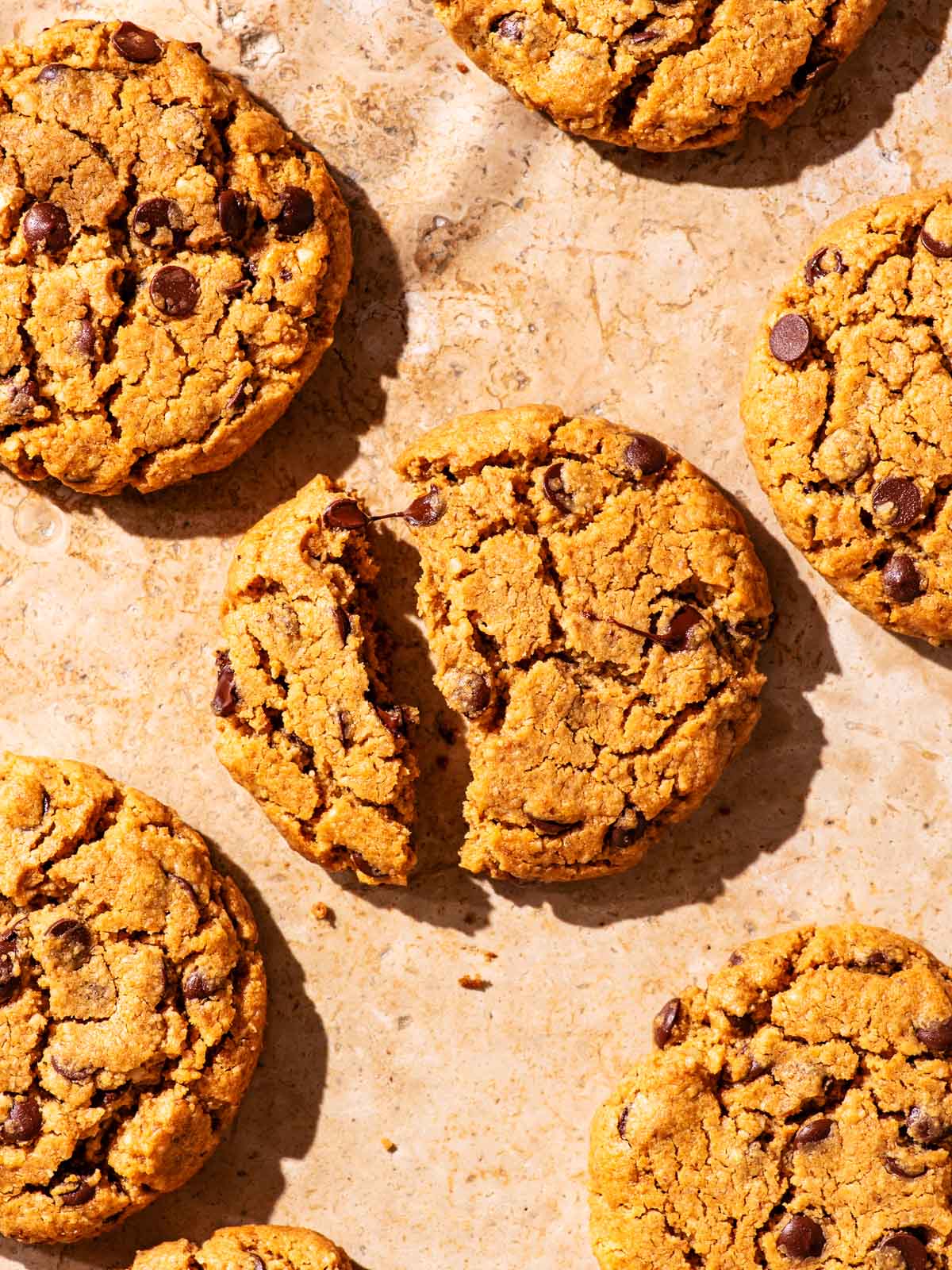 Several chocolate chip cookies on parchment paper, one broken in half.