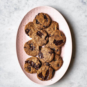 Several chocolate chunk cookies on a large pink serving platter.