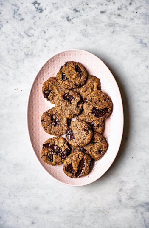 Several chocolate chunk cookies on a large pink serving platter.